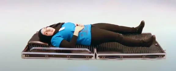 Presenter, Zayneb, lying on a bed of nails. Please don't try this at home - Our presenters are trained experts.