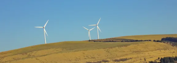 Three white windmills on green field under blue sky