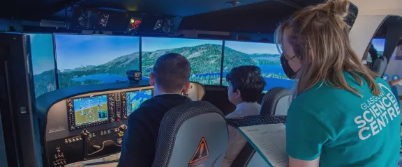 Two students at the controls of a flight simulator under instructor from science centre flight crew