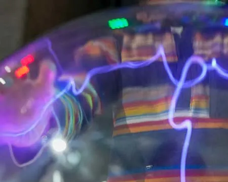 A hand placed on a plasma ball attracts a beam of purple-coloured particles