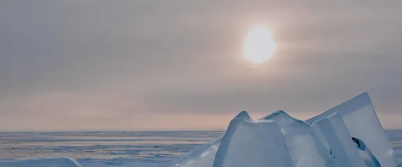 Shards of ice rise up from a frozen lake towards the hazy sunshine piercing the sky