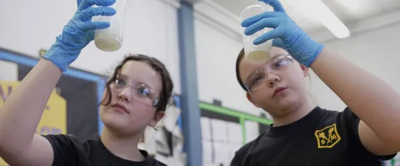 Two pupils raise a container to examine the contents of their experiment