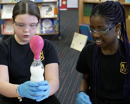 Two pupils in the classroom conduct an experiment to collect carbon dioxide gas in a balloon attached to a bottle.