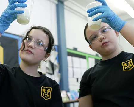 Two pupils hold up the result of an experiment in a small container