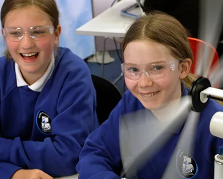 Two girls smile as they experiment with making a model wind turbine