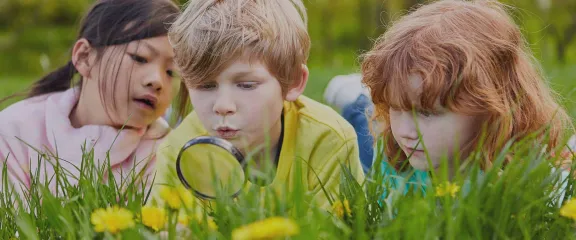 Young people looking at grass and flowers through a magnifying glass