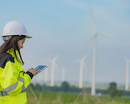 An engineer holds a tablet in front of wind turbines