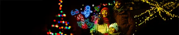 Family of 3, standing by a christmas tree and excitedly looking at neon light icons of presents, astronauts and rockets