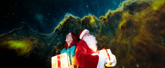 A woman and Santa hold glowing presents, while looking up at the planetarium 