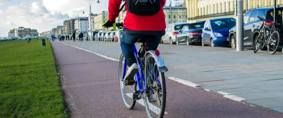 A cyclist in a cycle lane alongside a road in the city on one side and grass on the other