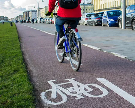 A cyclist in a cycle lane alongside a road in the city on one side and grass on the other