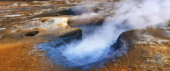 Steam rises from a hole in a volcanic landscape