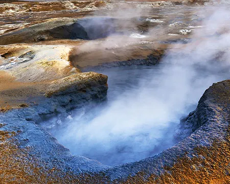 Steam rises from a hole in a volcanic landscape