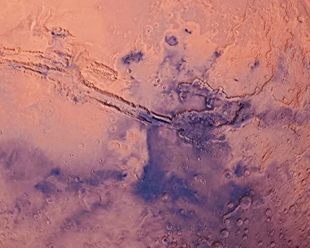 Scars on the surface of planet Mars appear as dark canyons against a lighter, red-coloured landscape.