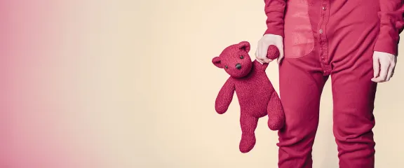 A child in red pyjamas carries a red teddy bear