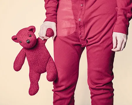 A child in red pyjamas carries a red teddy bear