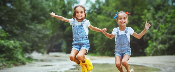 Two twin sisters jump in a muddy puddle.