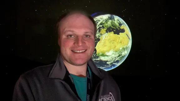 Planetarium presenter, Hayden, smiles while standing in front of the Earth displayed on the fulldome