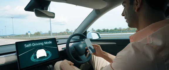 A man looks at a mobile phone behind the wheel of a self driving car on the motorway.