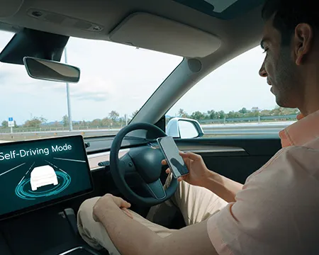 A man looks at a mobile phone behind the wheel of a self driving car on the motorway.