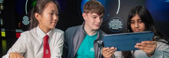 Pupils and a science communicator explore the results of an experiment on a tablet in the space zone